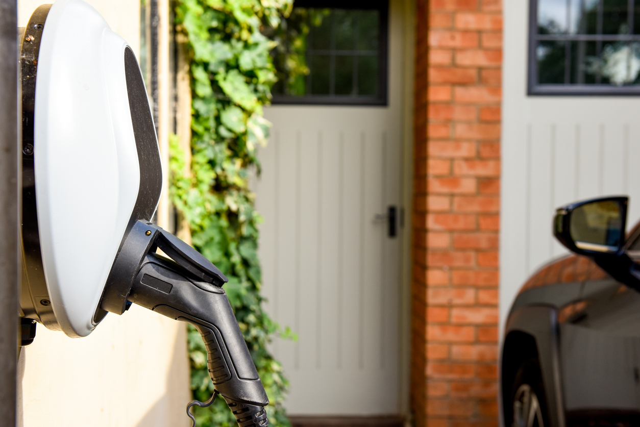 Electric vehicle charging at home wall charger near brick building.