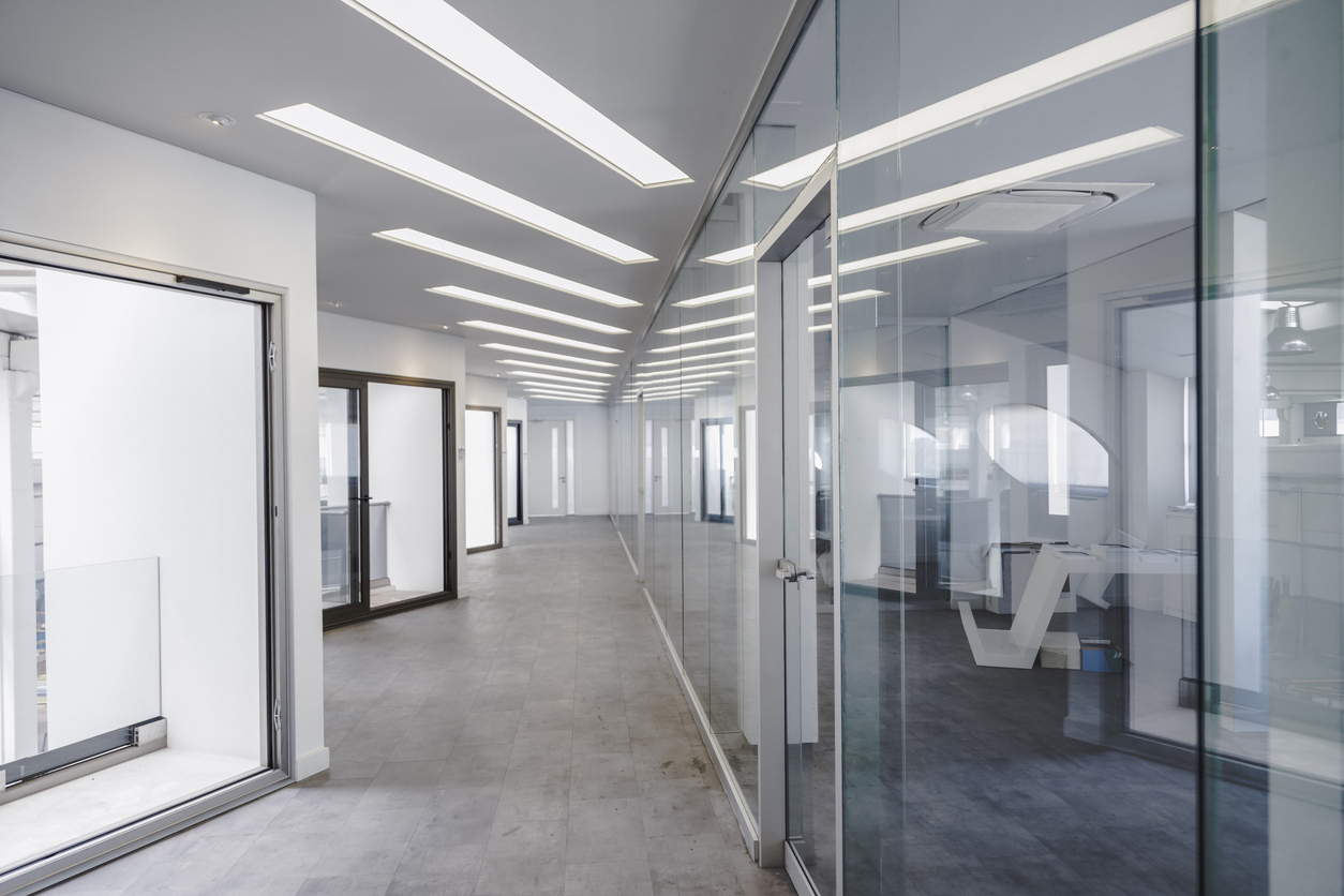 Modern office corridor with glass walls and bright lighting.