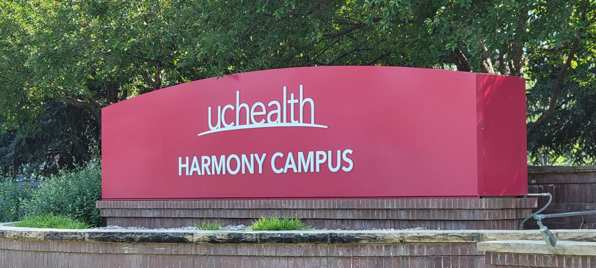Red UCHealth Harmony Campus sign surrounded by greenery.