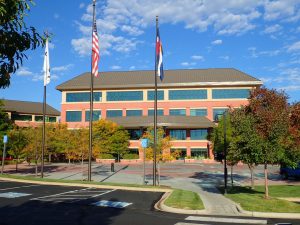 A brick office building with flags and trees in the foreground under a blue sky.