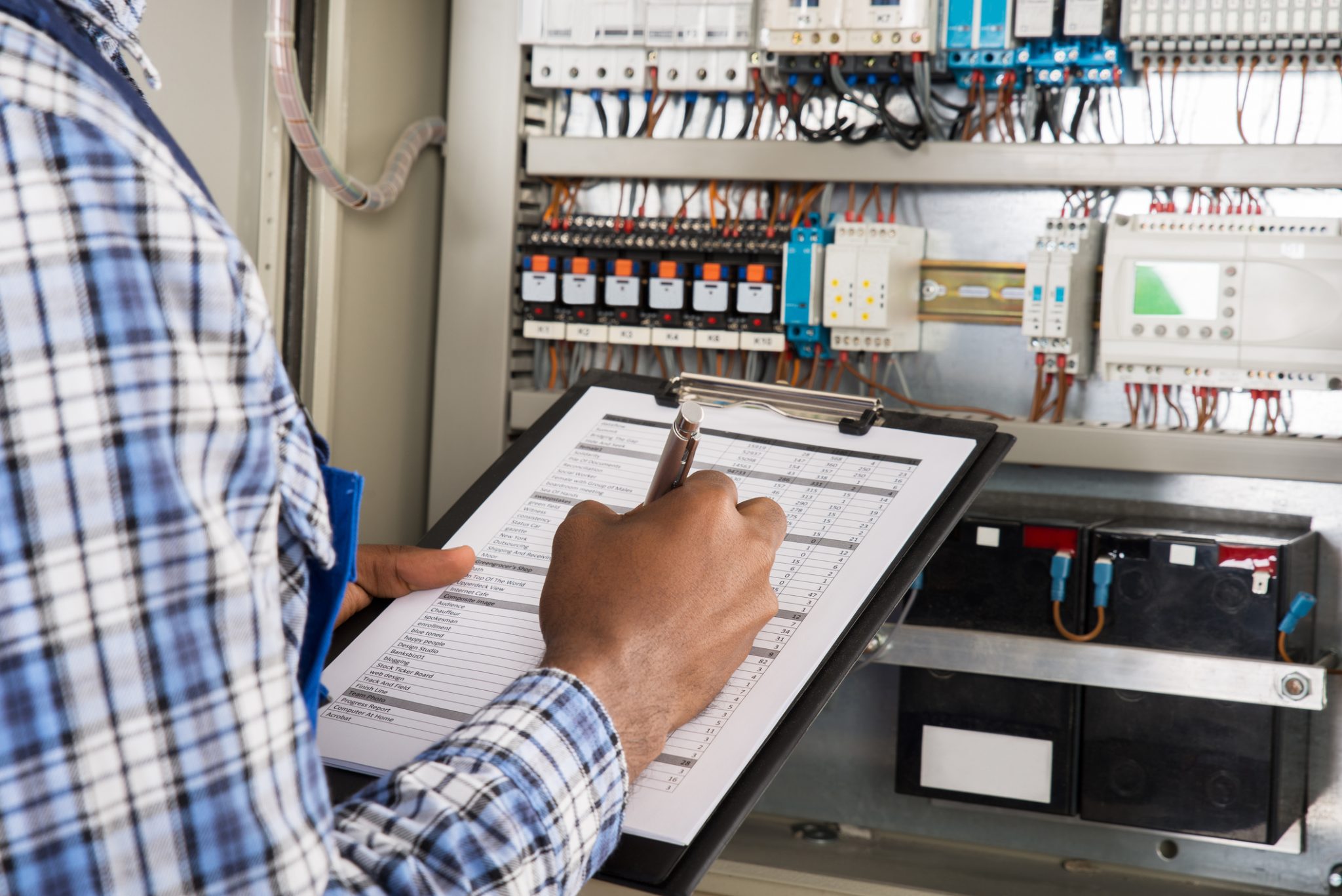 A Mac Electric NFPA specialist inspects a commercial electrical panel with clipboard for NFPA 70B maintenance documentation.