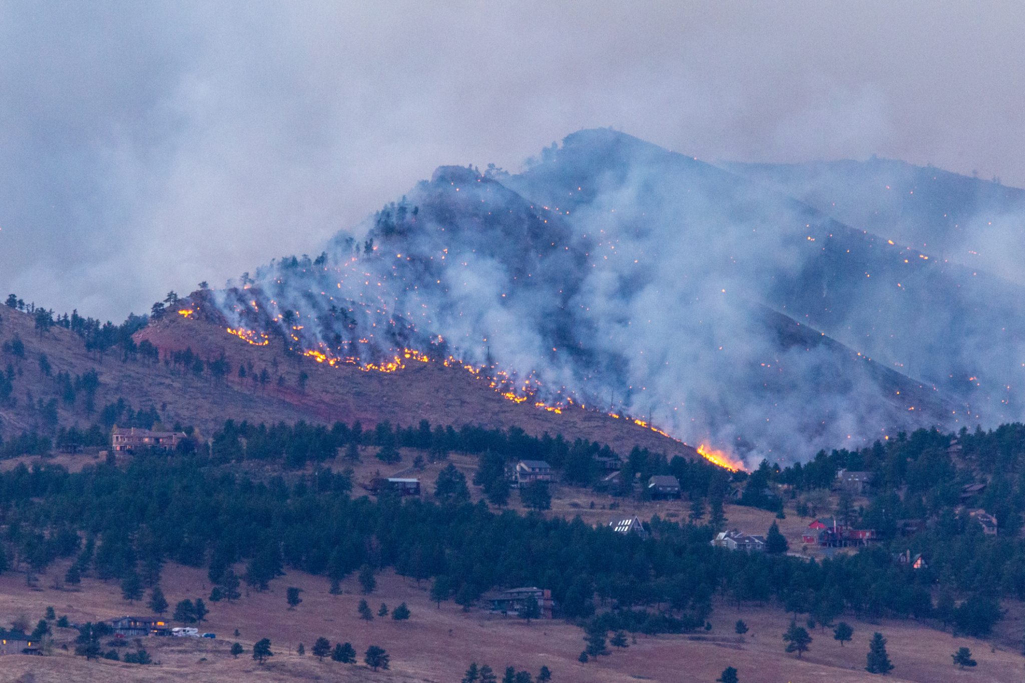 A wildfire burns near homes in the Colorado foothills, highlighting the need for backup generator installation.