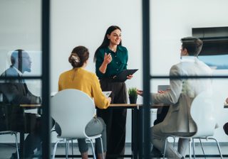 A woman leads a business meeting in a modern conference room with four colleagues present.
