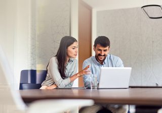 Colleagues discussing work on a laptop in a modern office setting.