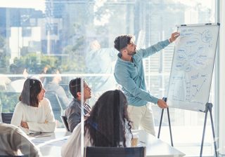 A man presenting a business strategy on a whiteboard to a group in a conference room.