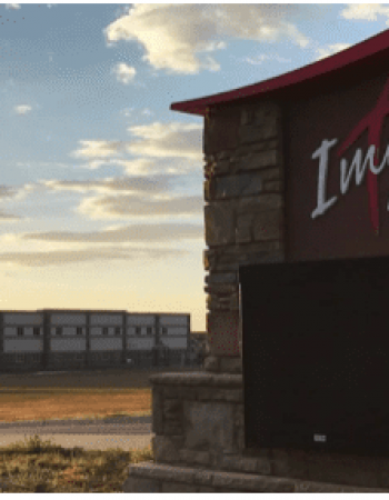 A large sign for Immanuel Lutheran Church and School stands in the foreground, illuminated by LED parking lot lights; in the background, buildings sit under a partly cloudy sky at sunset.